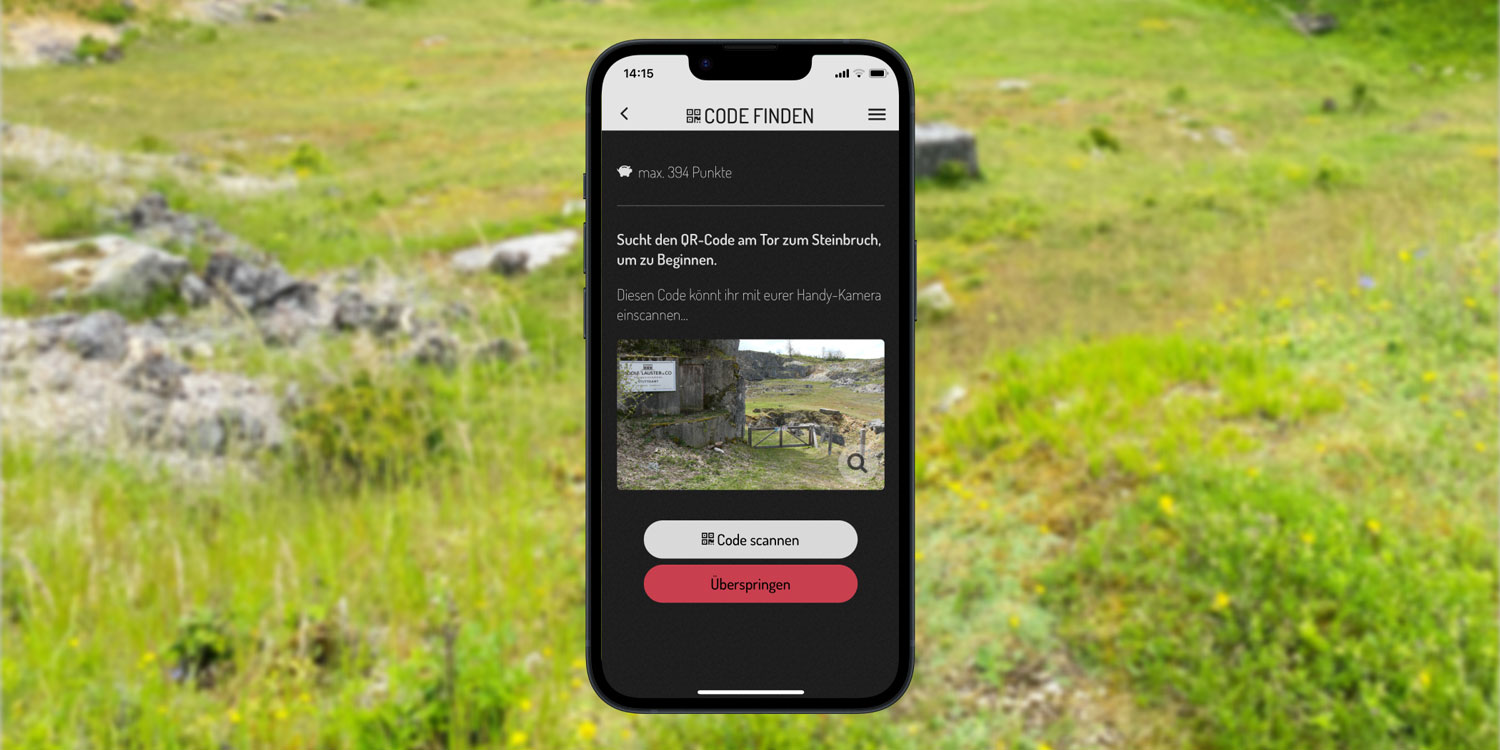 Screenshot der Actionbound-App mit Aufgabe einen Code zu finden vor dem Hintergrund einer Wiese