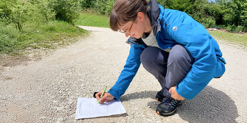 Junge Frau macht unseren Geocache und füllt das zugehörige Rätsel aus.